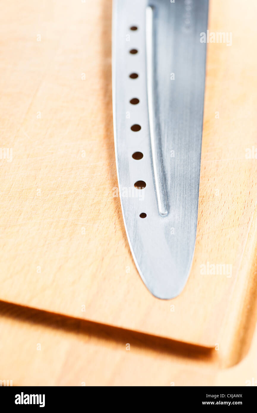 Knife with holes lying on wooden cutting board Stock Photo Alamy