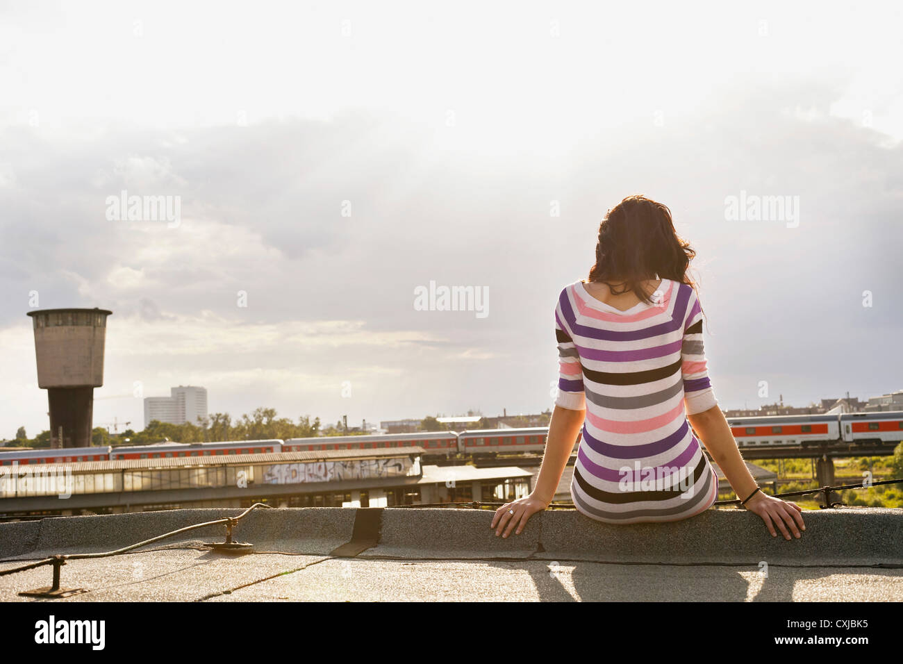 Germany, Hamburg, Young woman sitting at edge of roof Stock Photo