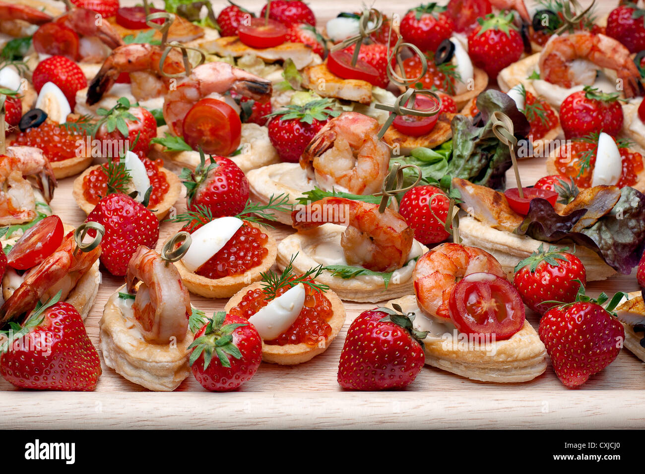 Lot of canape with shrimp, caviar, strawberries and other on wooden tray, selective focus Stock Photo
