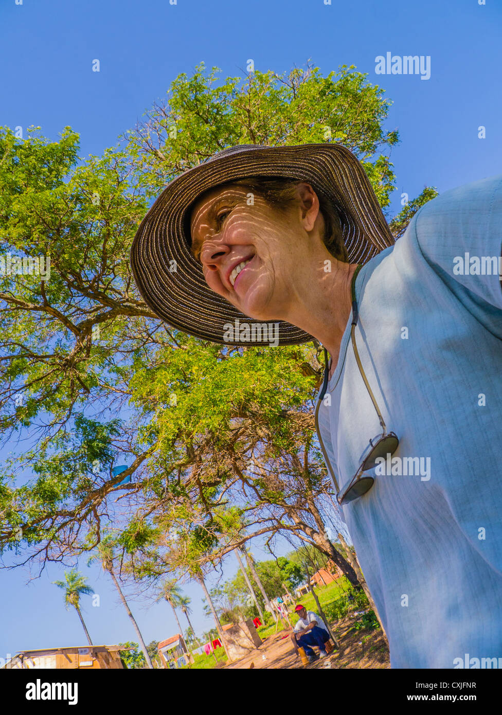 A Habitat for Humanity Paraguay volunteer, a middle-aged Caucasian woman smiles standing outside under a tree and deep blue sky. Stock Photo