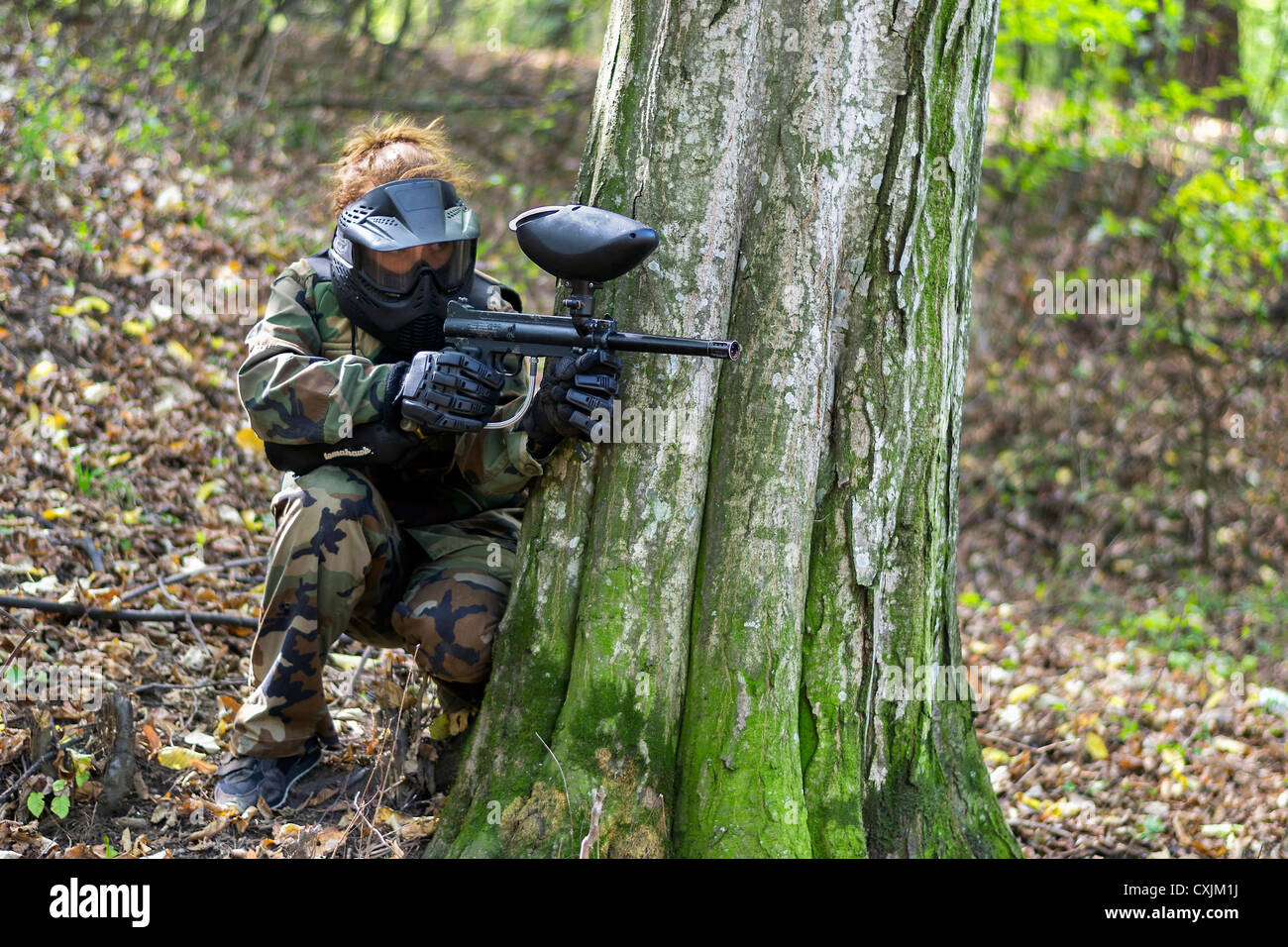 Girl in camo taking cover behind a tree during a paintball tournament