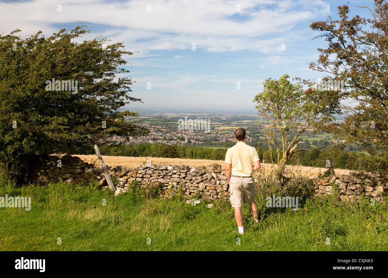 Senior man looks at views over Winchcombe from the barrow at Belas Nap in English Cotswolds Stock Photo