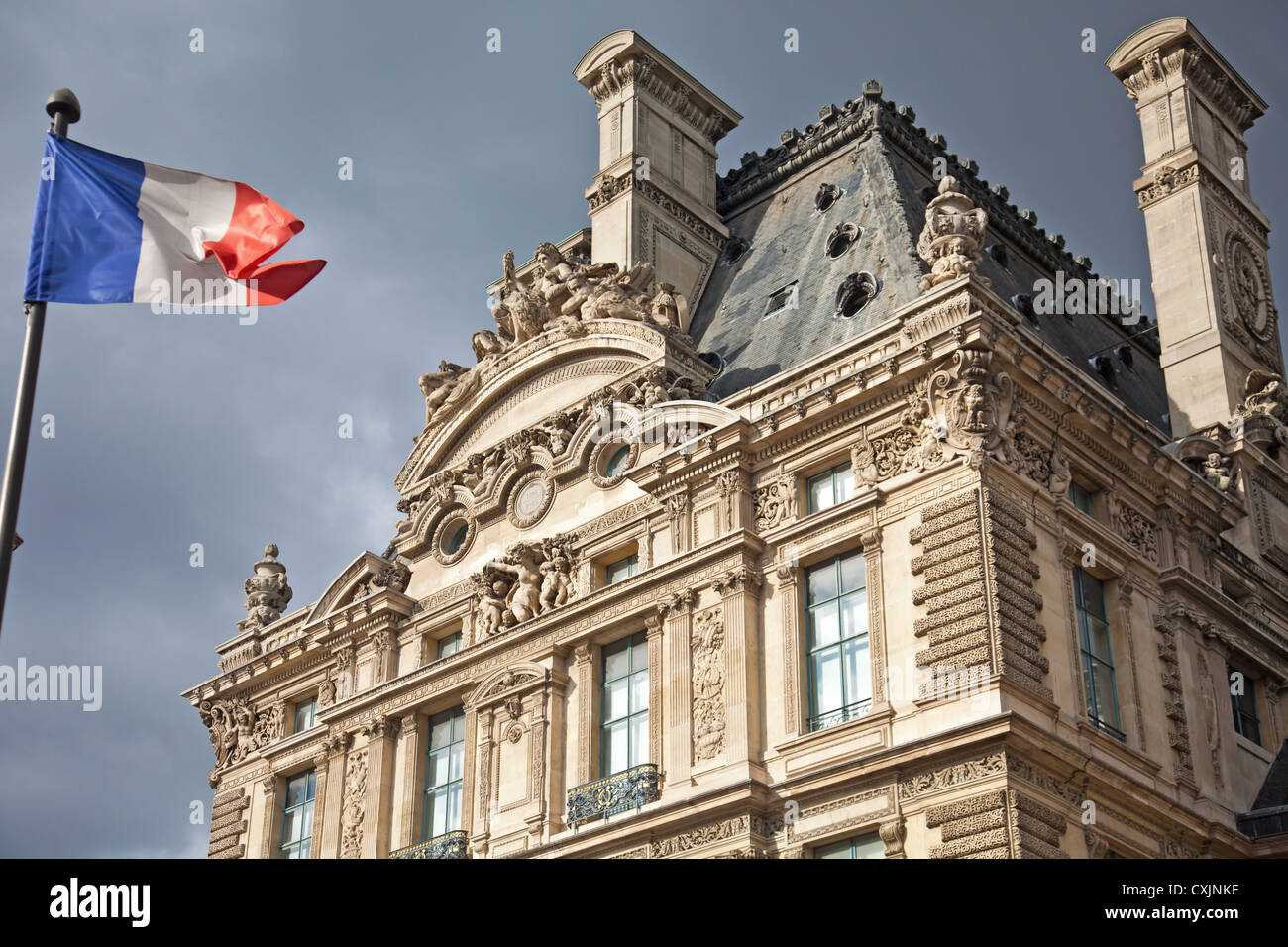 French Flag (tricolor) flying in front of a section of the Musée du Louvre, France's best known and largest museum & Art Gallery Stock Photo