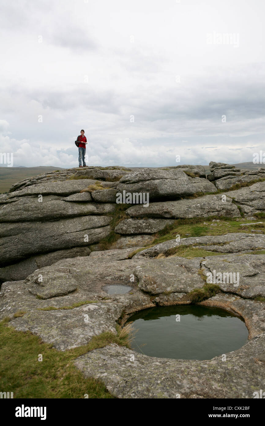 Water filled rock pool on Kestor Rock, with man in background, Dartmoor National Park, cloudy overcast day Stock Photo