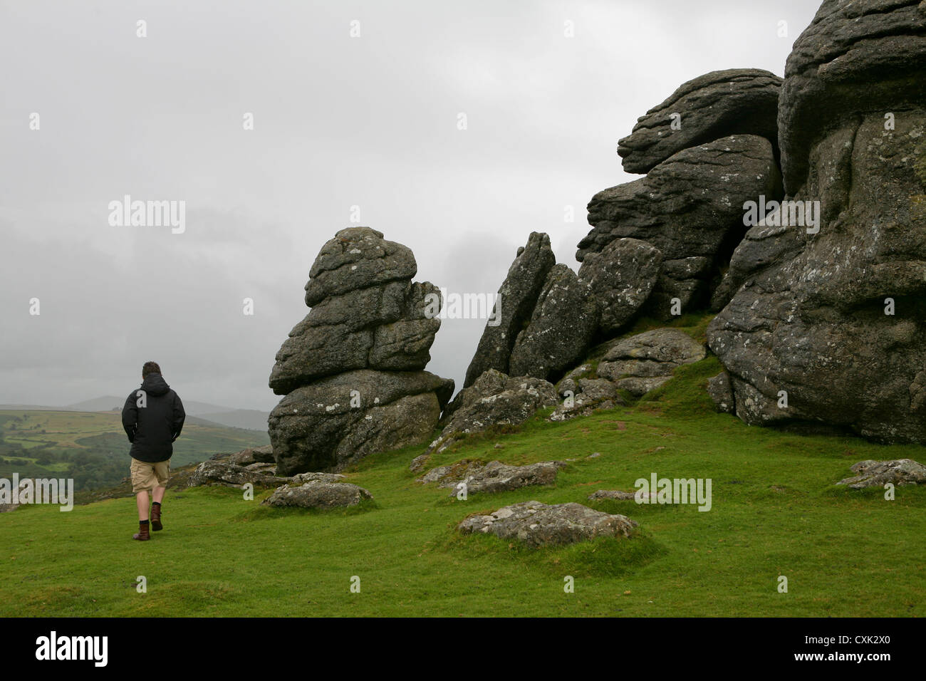 Man walking by rocky outcrop of Saddle Tor, Dartmoor, on an overcast, wet and windy day Stock Photo