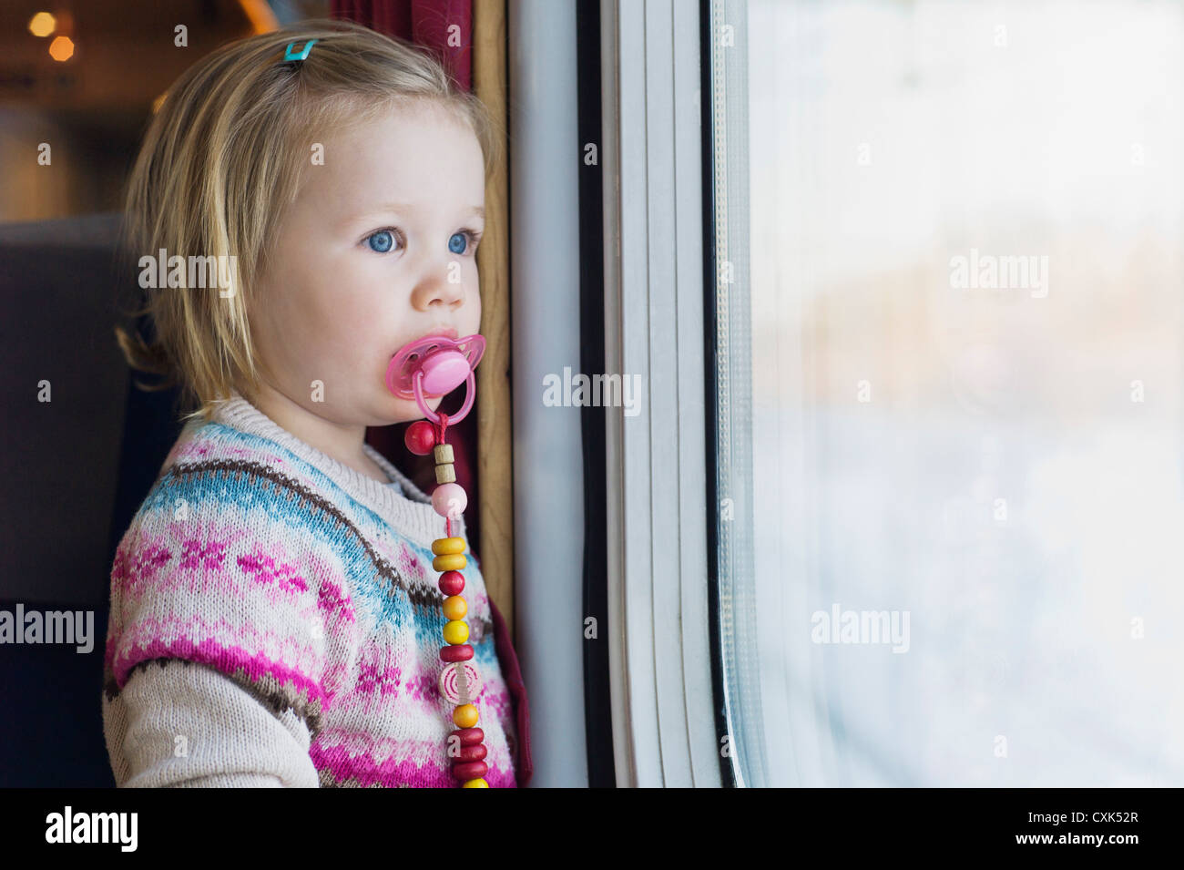 Portrait of Little Girl using Pacifier and Looking out Train Window Stock Photo