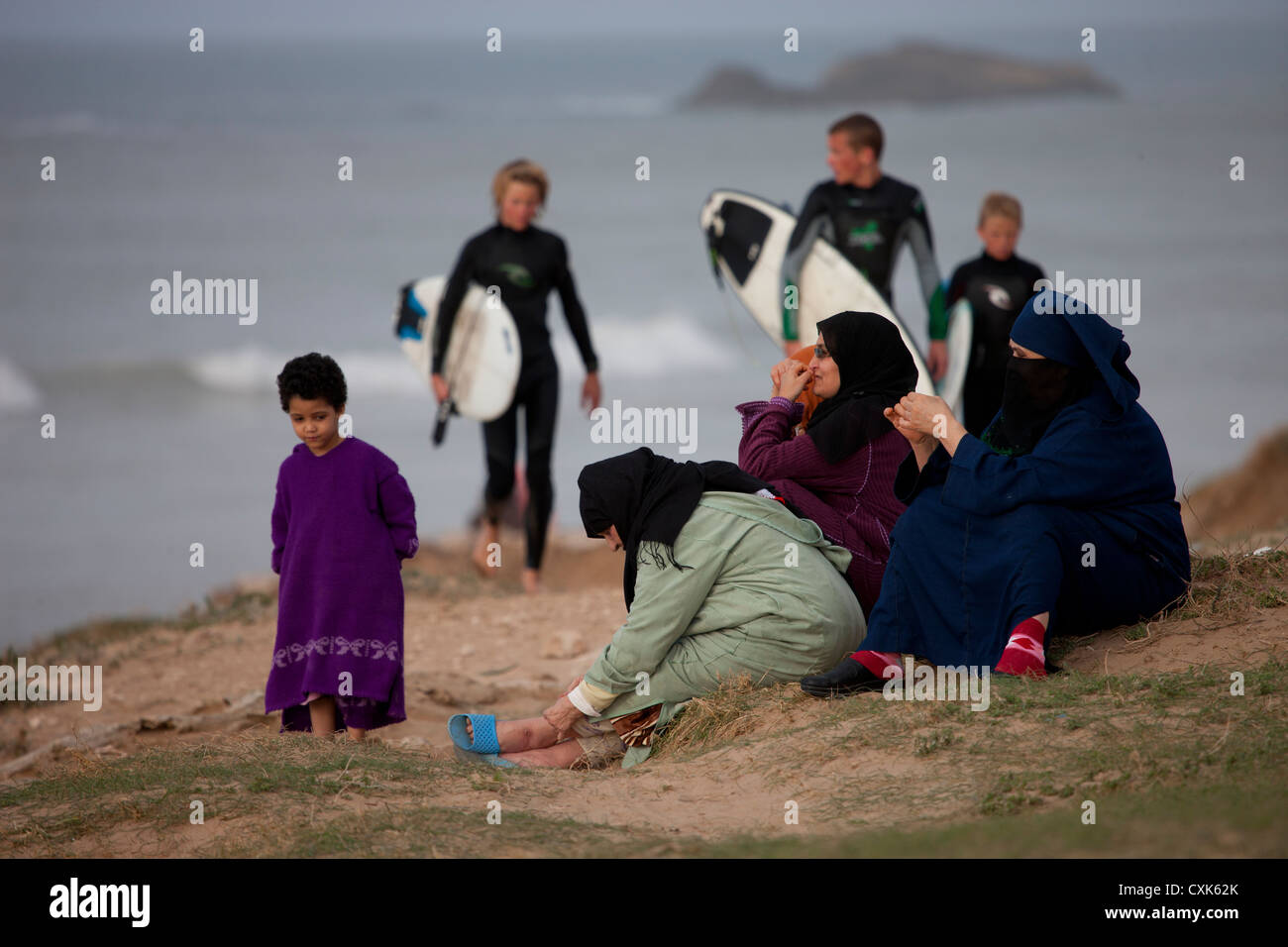 Local Moroccans and child with surfers in background on the beach, Essaouira, Morocco. Stock Photo