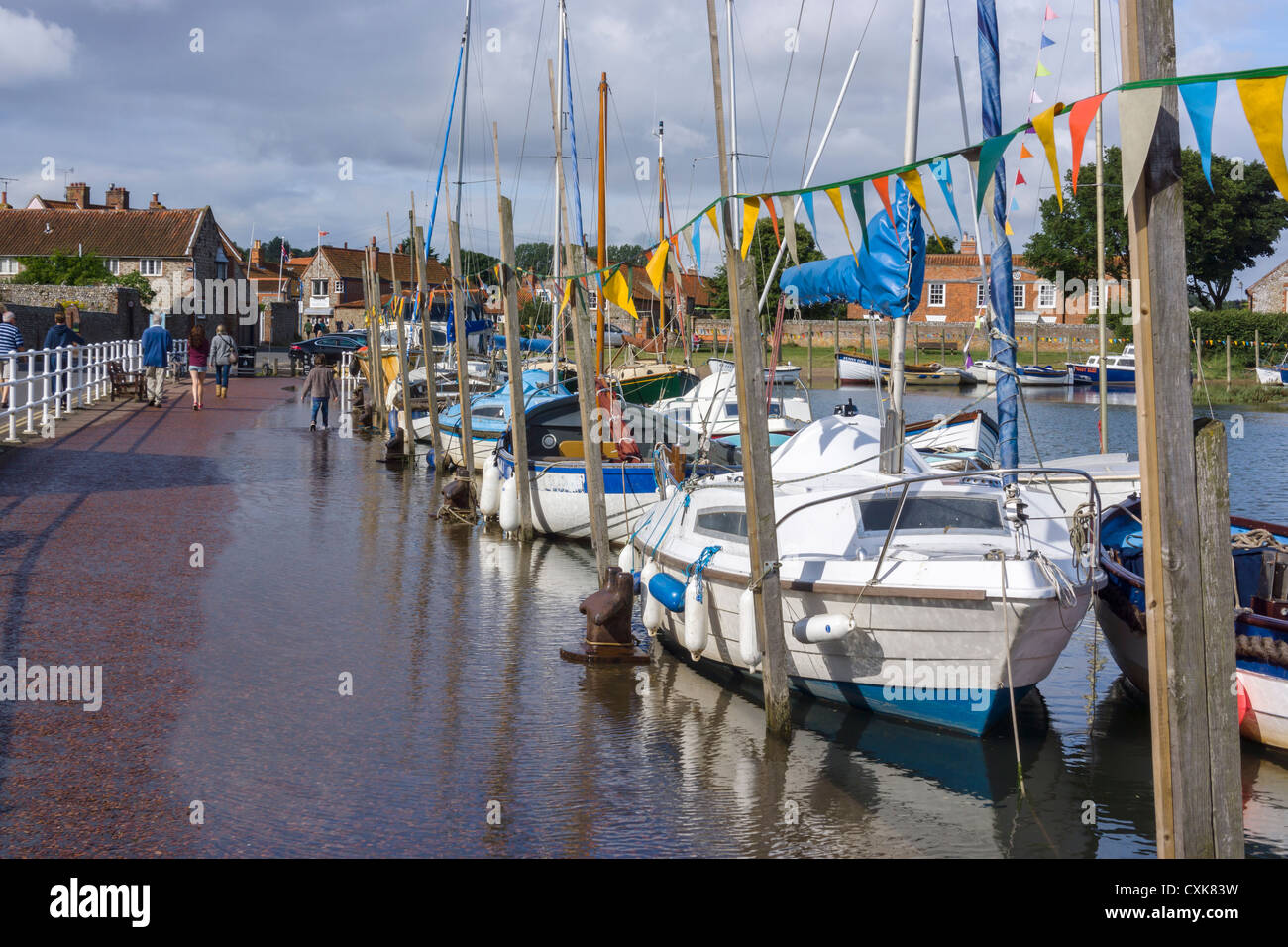 Boats moored in Blakeney harbour at high tide with the sea encroaching on the pavement. Stock Photo