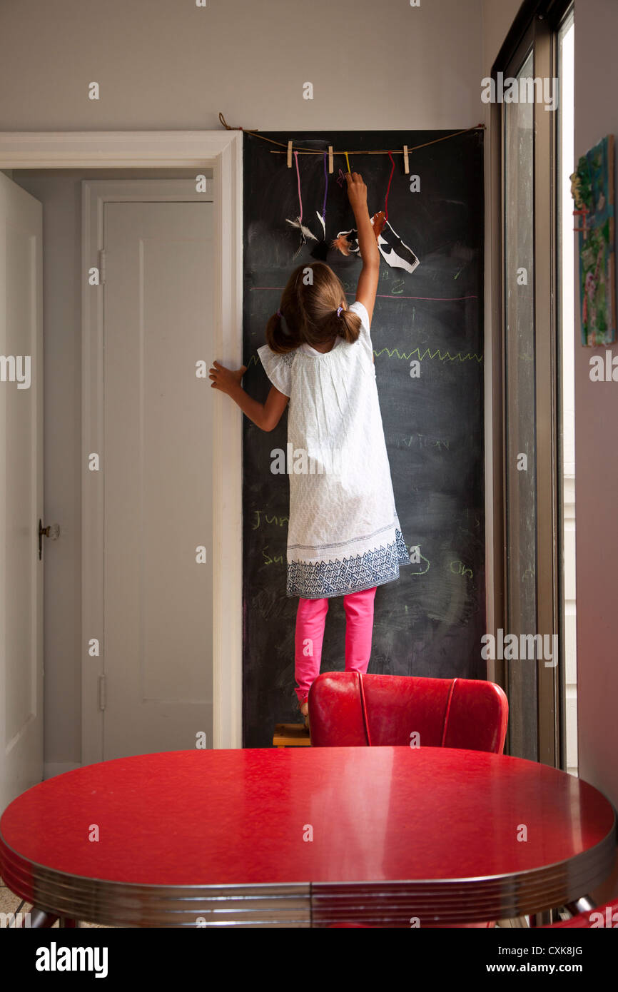 A six year old is in a kitchen writing on a black chalkboard Stock
