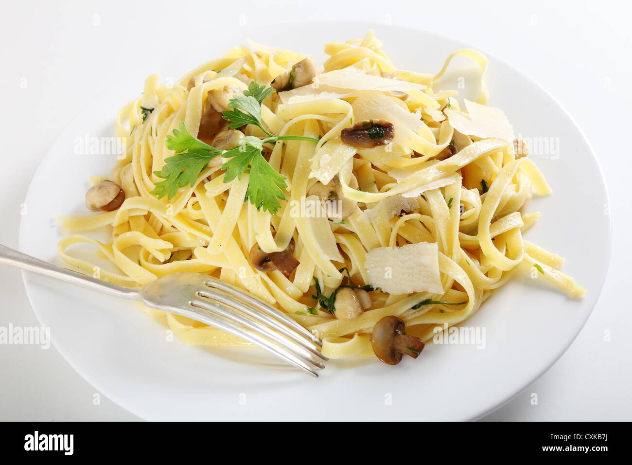 Ribbon pasta with mushrooms and italian parsley, fettuccine ai funghi, topped with curls of parmesan reggiano and with a fork Stock Photo