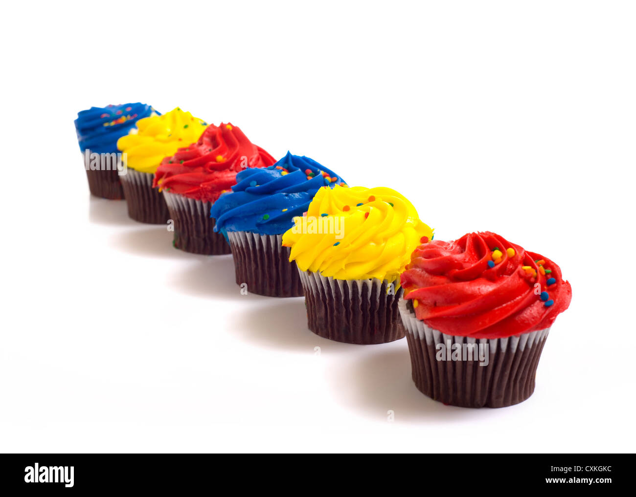 A row of bright, primary colored chocolate cupcakes on a white background Stock Photo