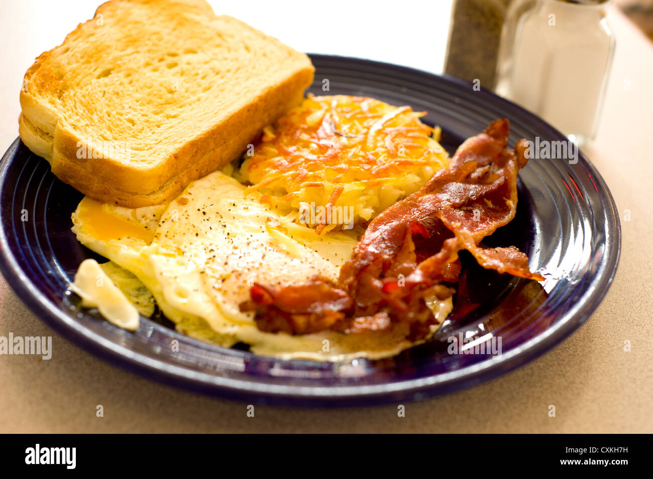 A savory American breakfast at a restaurant with egg, bacon, hash brown and toast on a blue