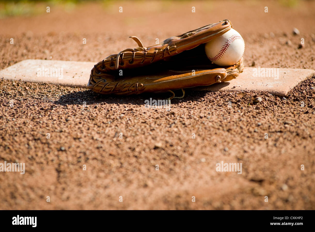 A brown leather baseball glove and a white leather baseball on a pitcher's mound at a baseball field, with copy space Stock Photo