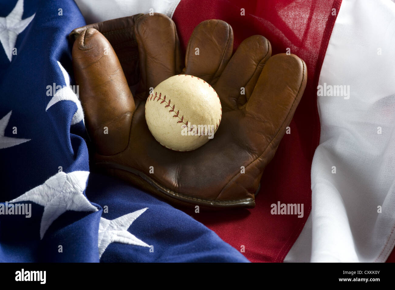 A grouping of classic baseball items including an antique glove or mitt and an antique baseball on top of an American Flag Stock Photo