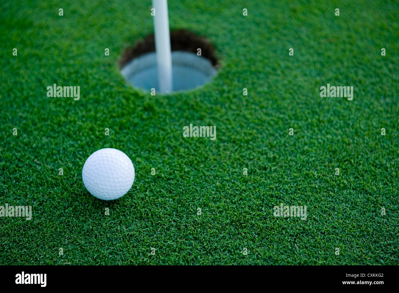 A white golf ball near the hole of a golfing green or course Stock Photo