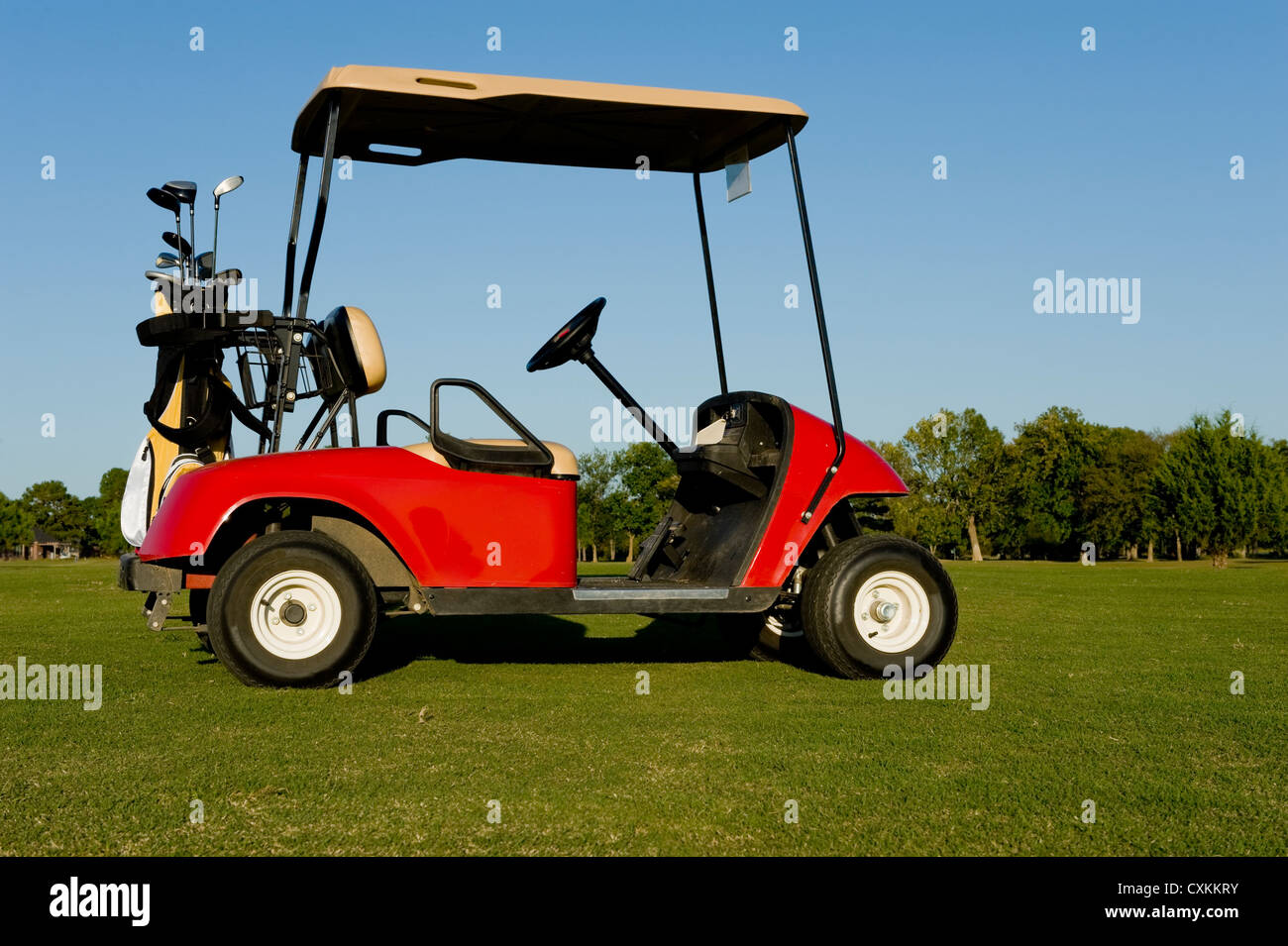 A red golf cart or buggy on a golf course with golf clubs etc Stock Photo