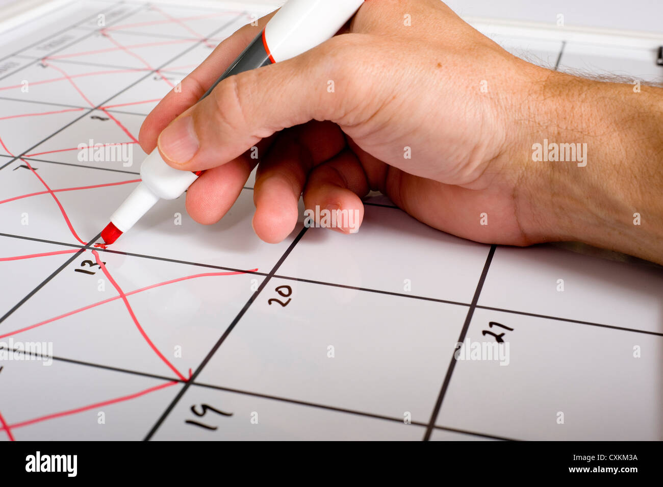 A hand holding a dry erase marker X'ing out or crossing out days of the