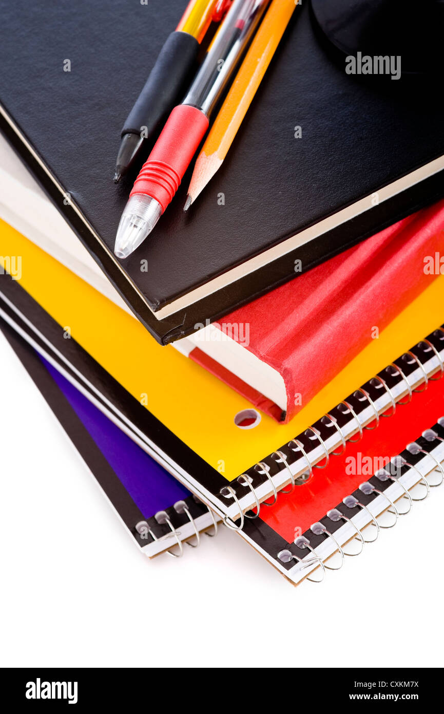 A stack of school books and spiral notebooks with a pencil and pens on tops in front of a white