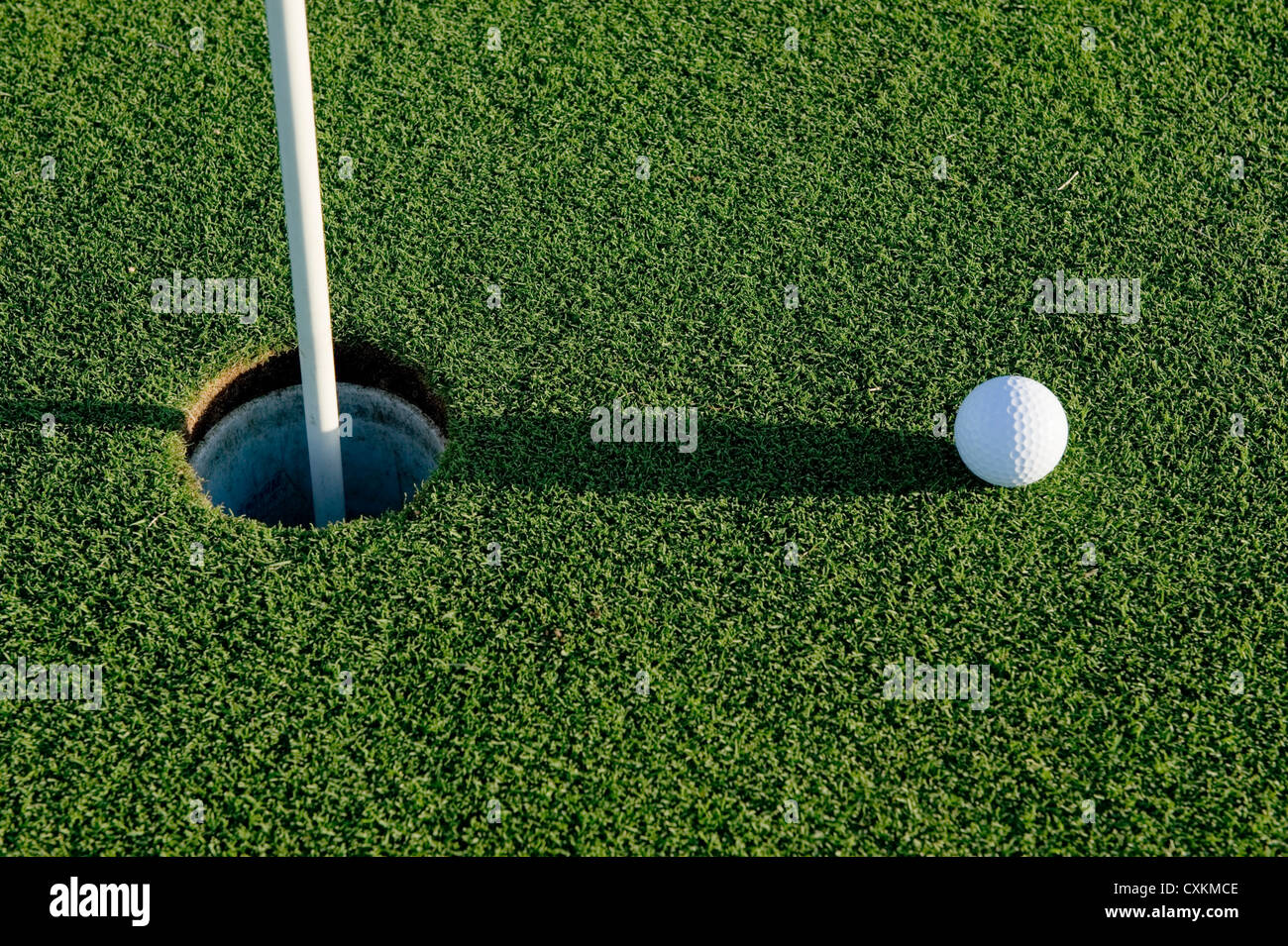 A white golf ball near the hole of a golfing green or course Stock Photo