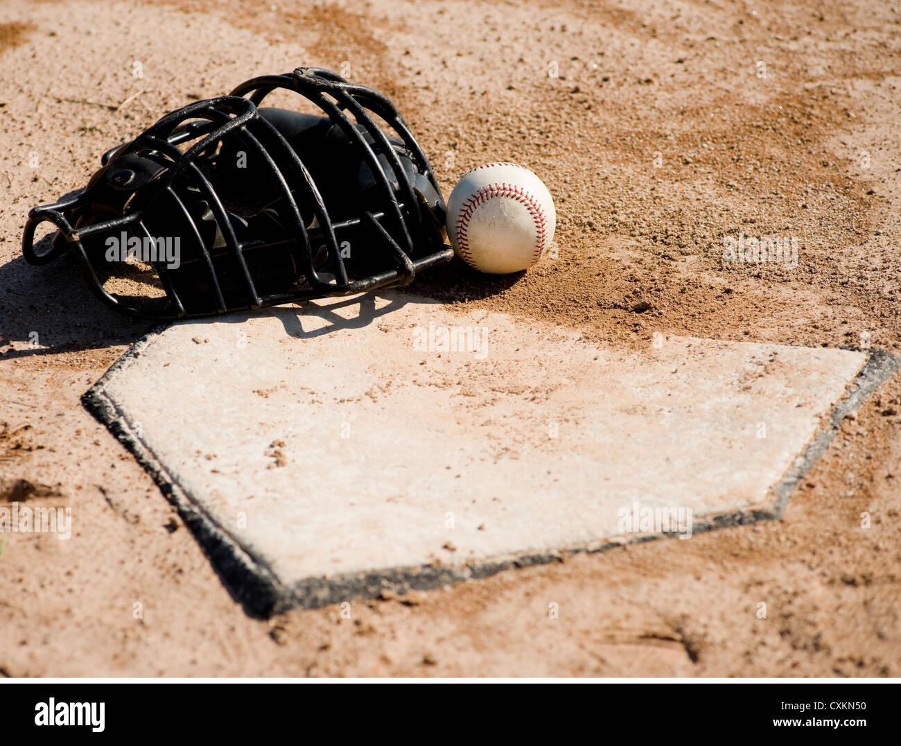 A baseball catcher's protective mask and baseball lying on home plate on a dirt baseball field Stock Photo