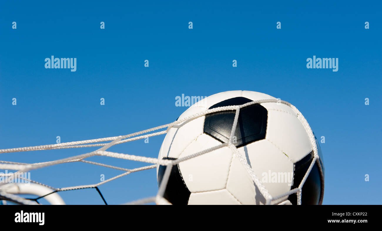 A traditional soccer ball or football in a goal net in front of a blue sky Stock Photo
