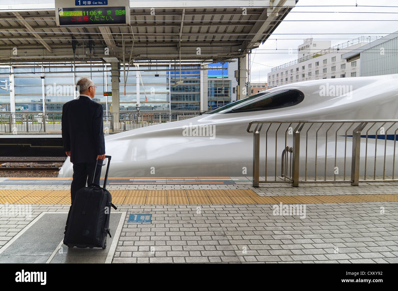 A passenger waits on a station platform as a bullet train arrives. Stock Photo