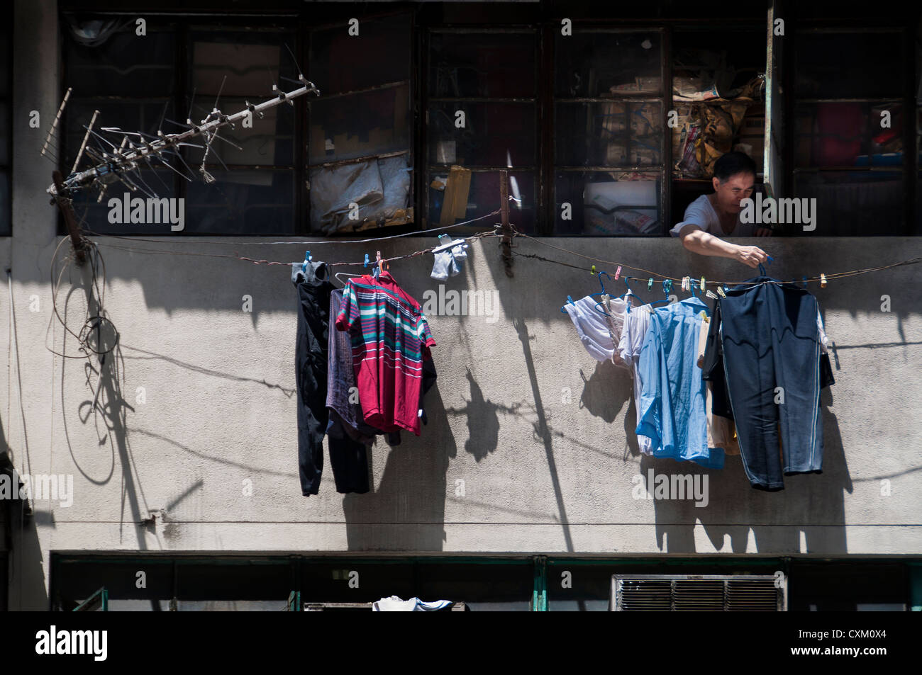 Man hanging laundry from his apartment window, Hong Kong Stock Photo