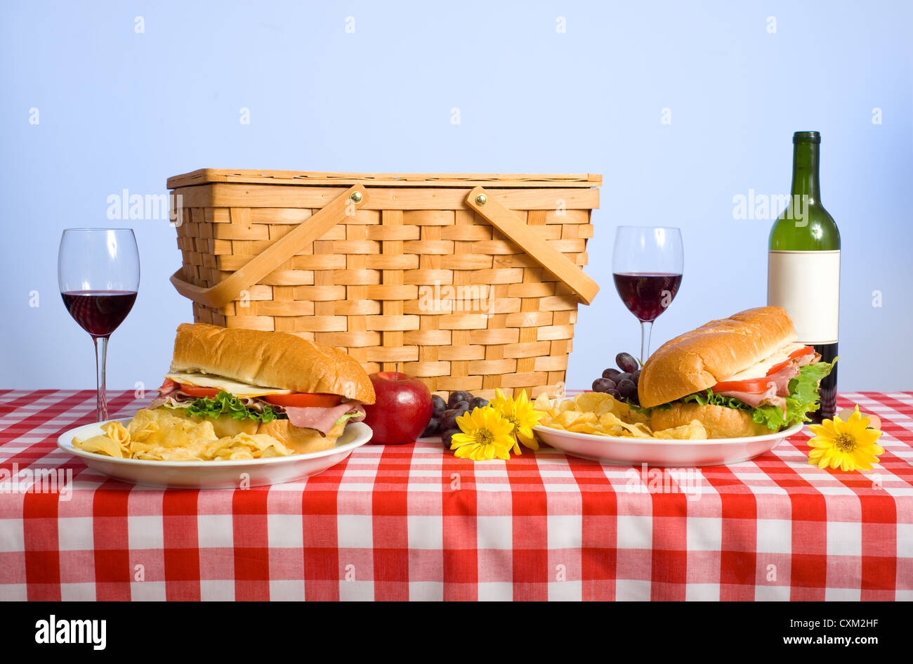 Picnic lunch on a red gingham tablecloth including wicker basket and wine glasses with
