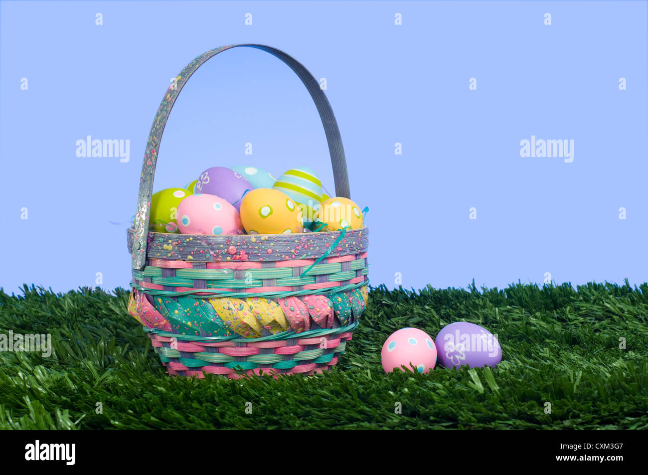 Brightly colored Easter eggs in a basket on grass with a blue sky background Stock Photo