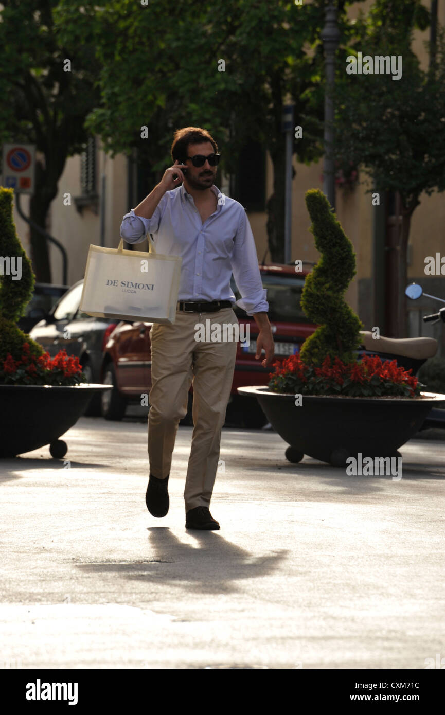 Fashionably dressed young man out shopping and talking on his mobile phone in Lucca Tuscany Italy Stock Photo