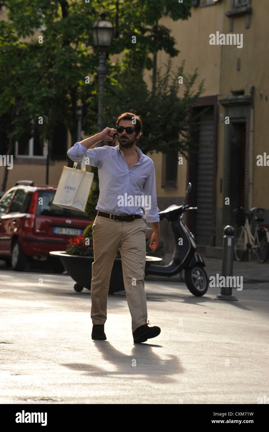 Fashionably dressed young man out shopping and talking on his mobile phone in Lucca Tuscany Italy Stock Photo