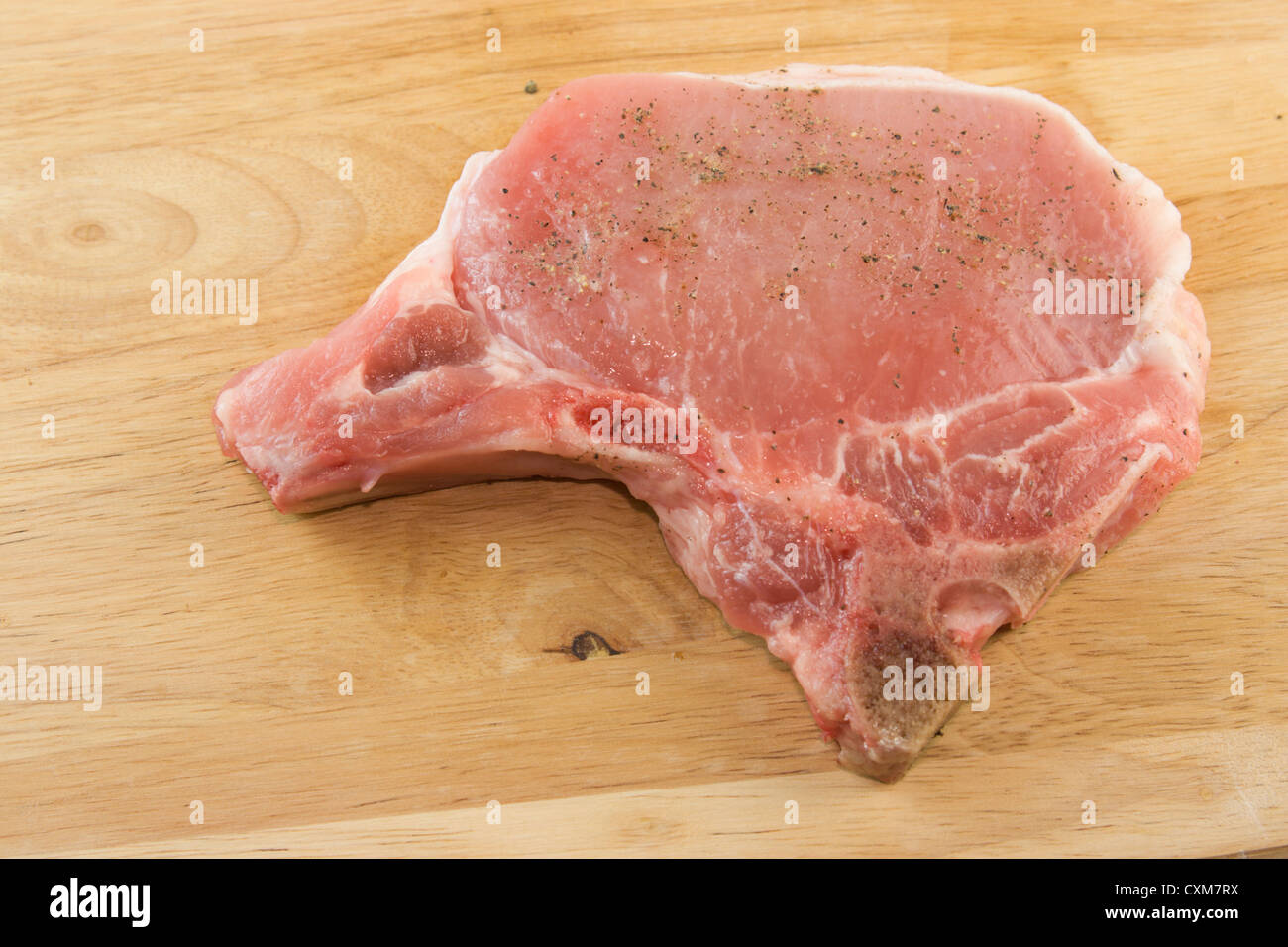 fresh, pork chop seasoned with salt and pepper on woodgrain cutting board ready to cook Stock Photo