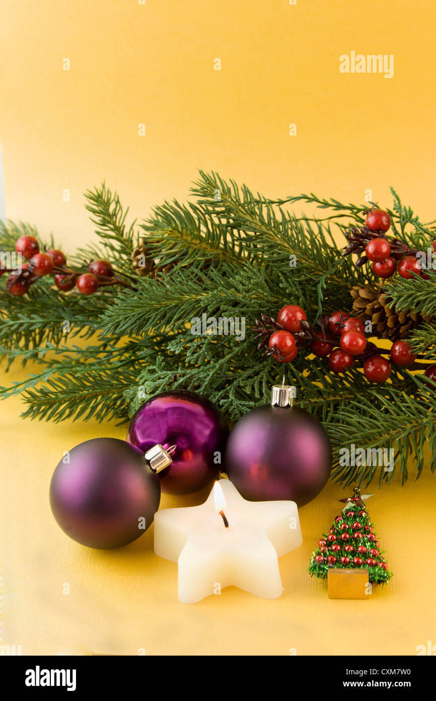 purple Christmas ornaments with star shaped candle, fir branch, holly berries on a soft gold background with copyspace Stock Photo