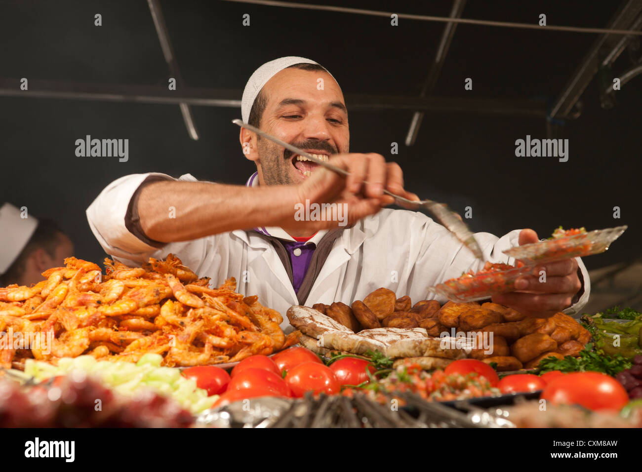 happy local serving up food in food stand market evening Jamaa el Fna Square in Marrakech, Morocco Stock Photo