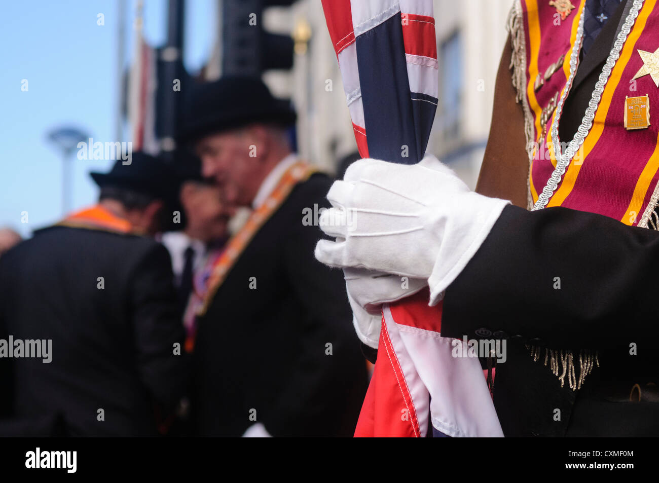 Orangeman wearing white gloves holds a furled Union Flag Stock Photo