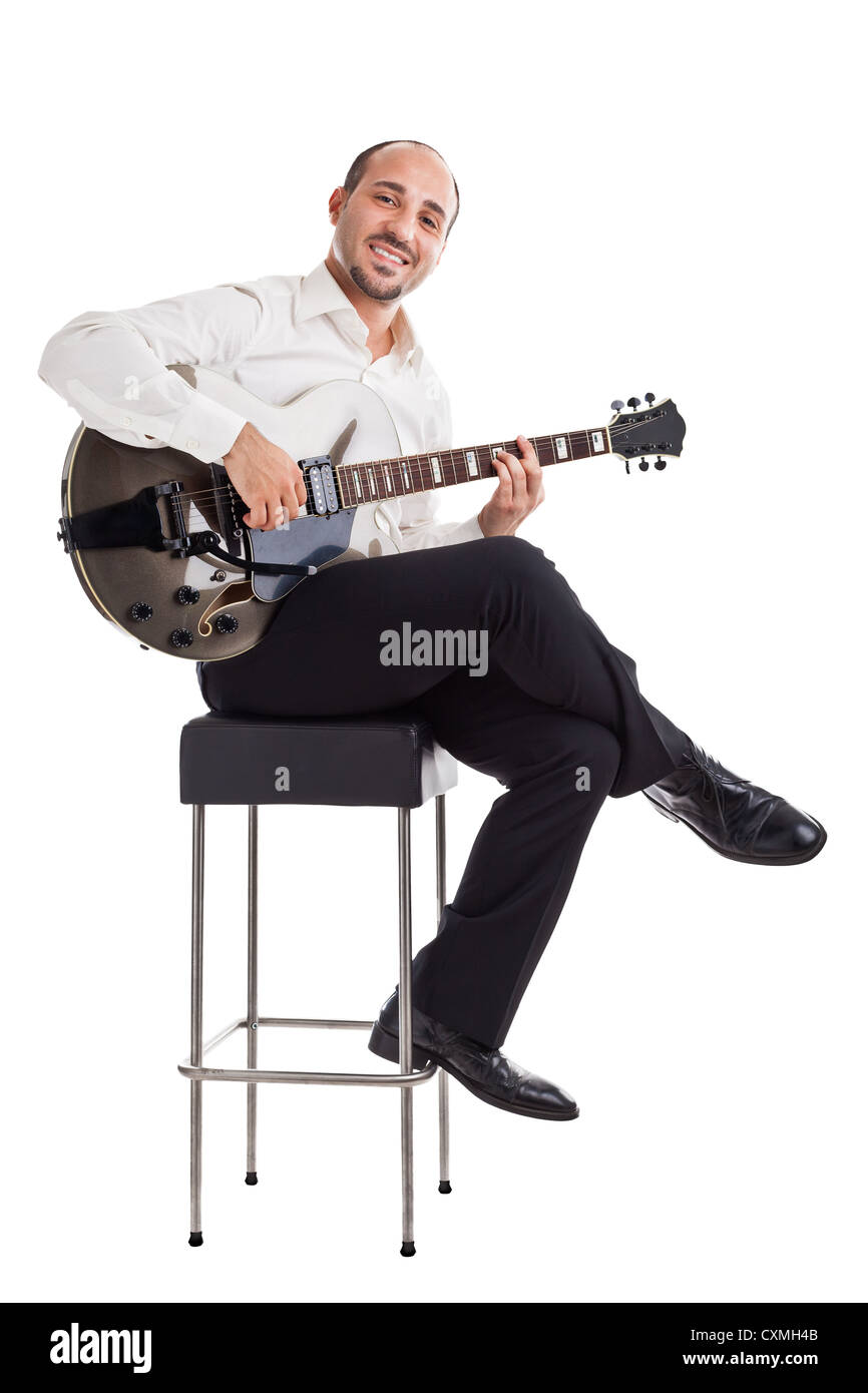 a well dressed jazz musician sitting on a stool and holding a guitar