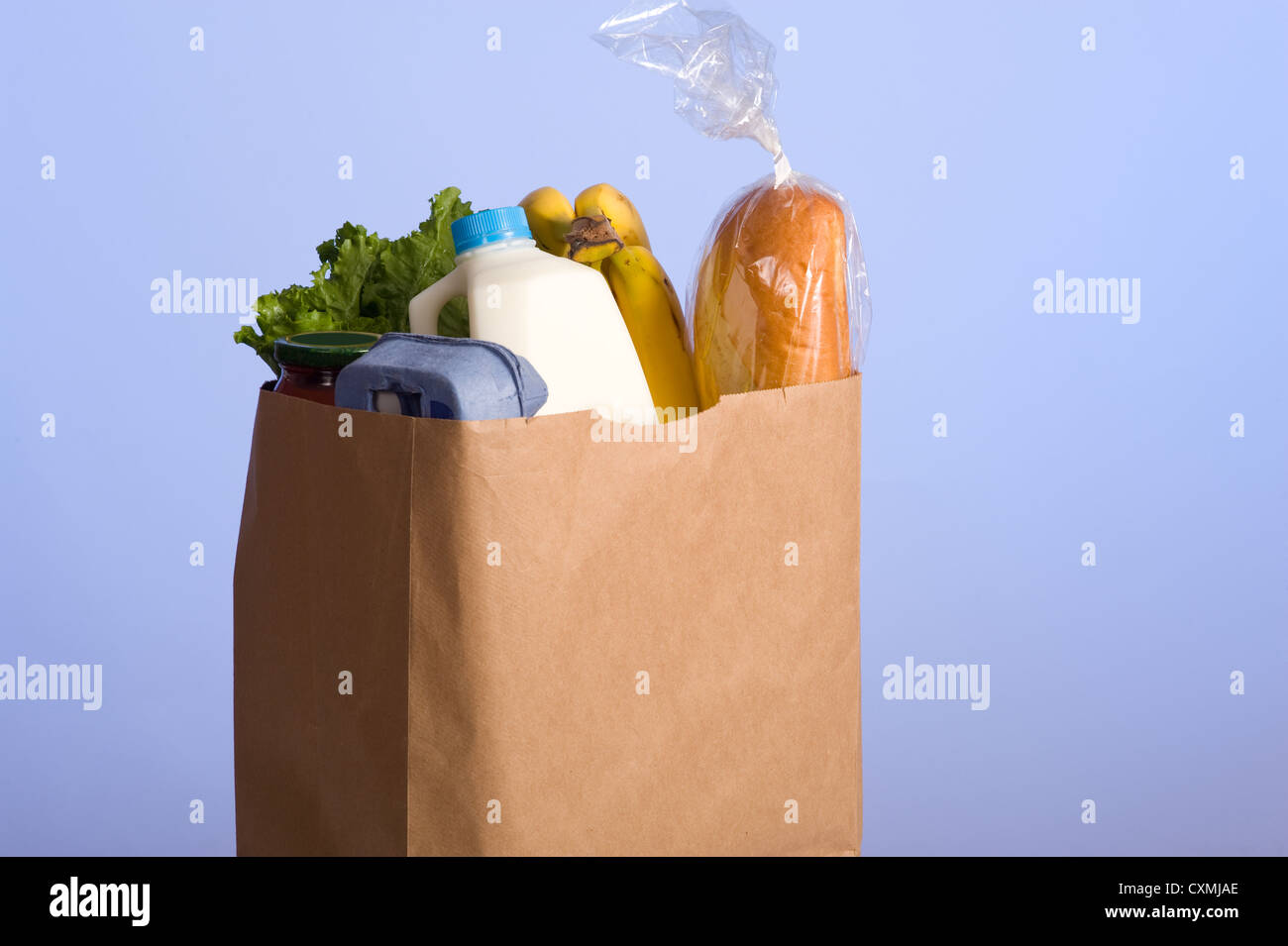 A brown paper bag full of groceries on a blue background, with bread, milk, eggs, pasta, lettuce and bananas. with copy space Stock Photo