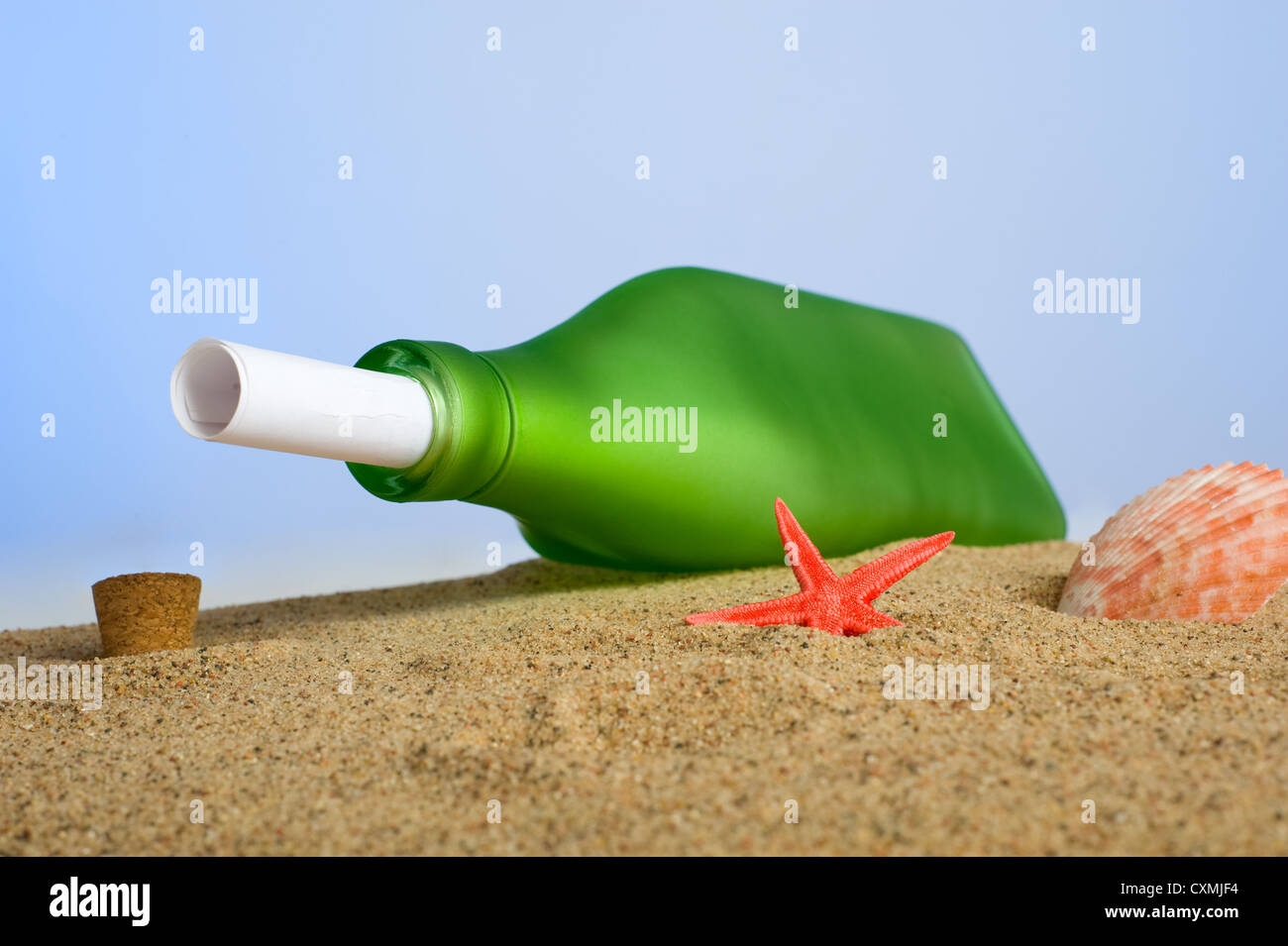 A rolled piece of paper in a green bottle on a sandy beach with sea shells etc, message in a bottle concept Stock Photo