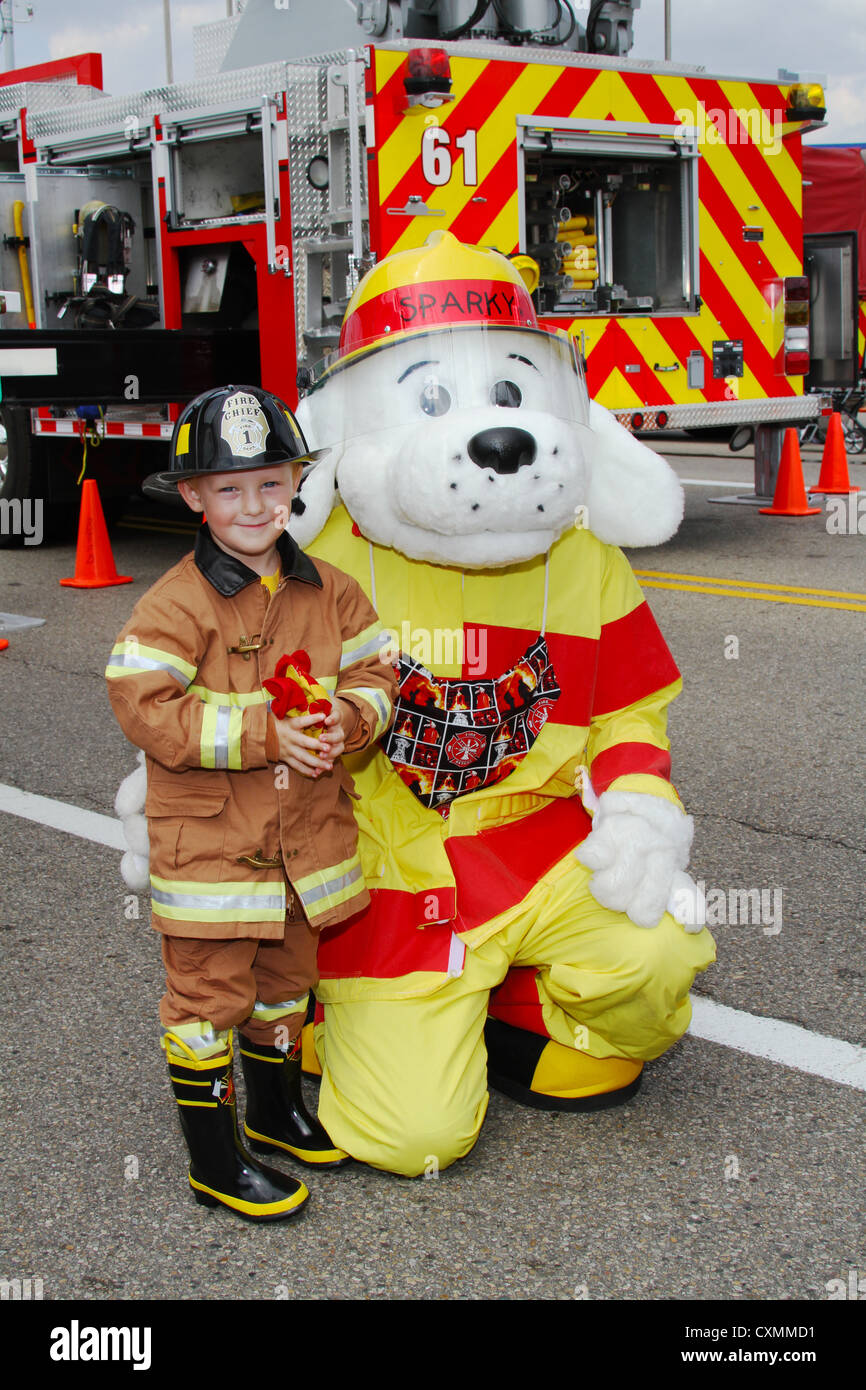 Young boy dressed in fire suit standing with Sparky the fire dog