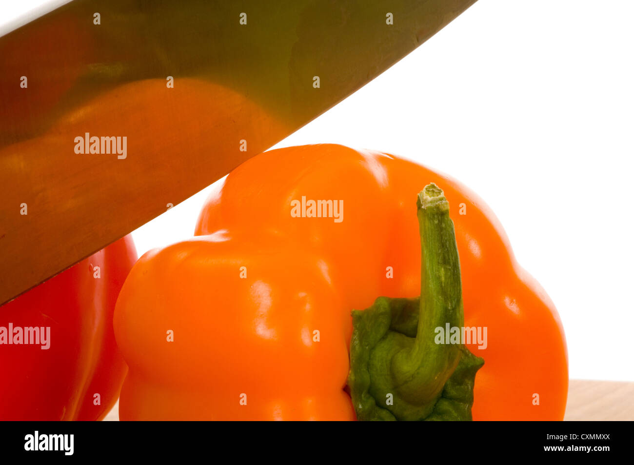 Red and orange bell peppers on cutting board with knife against white ...