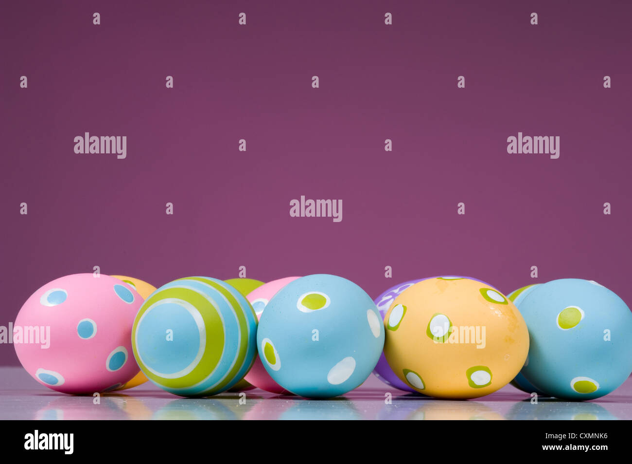Row of pastel decorated Easter eggs on a purple background with copy ...