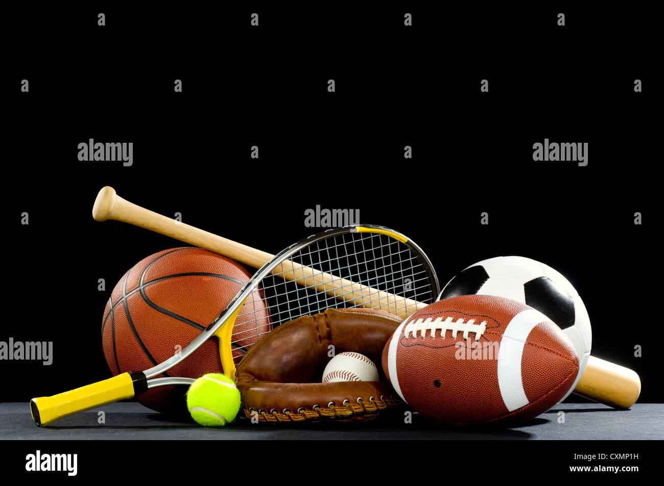 Assorted sports equipment including bat, baseball, football, soccer ball, basketball, tennis racket and ball on black Stock Photo