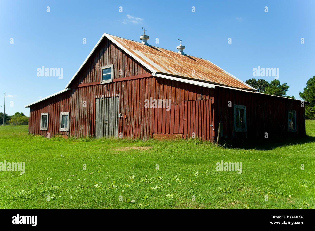Old red barn against blue sky with green grass in front Stock Photo - Alamy