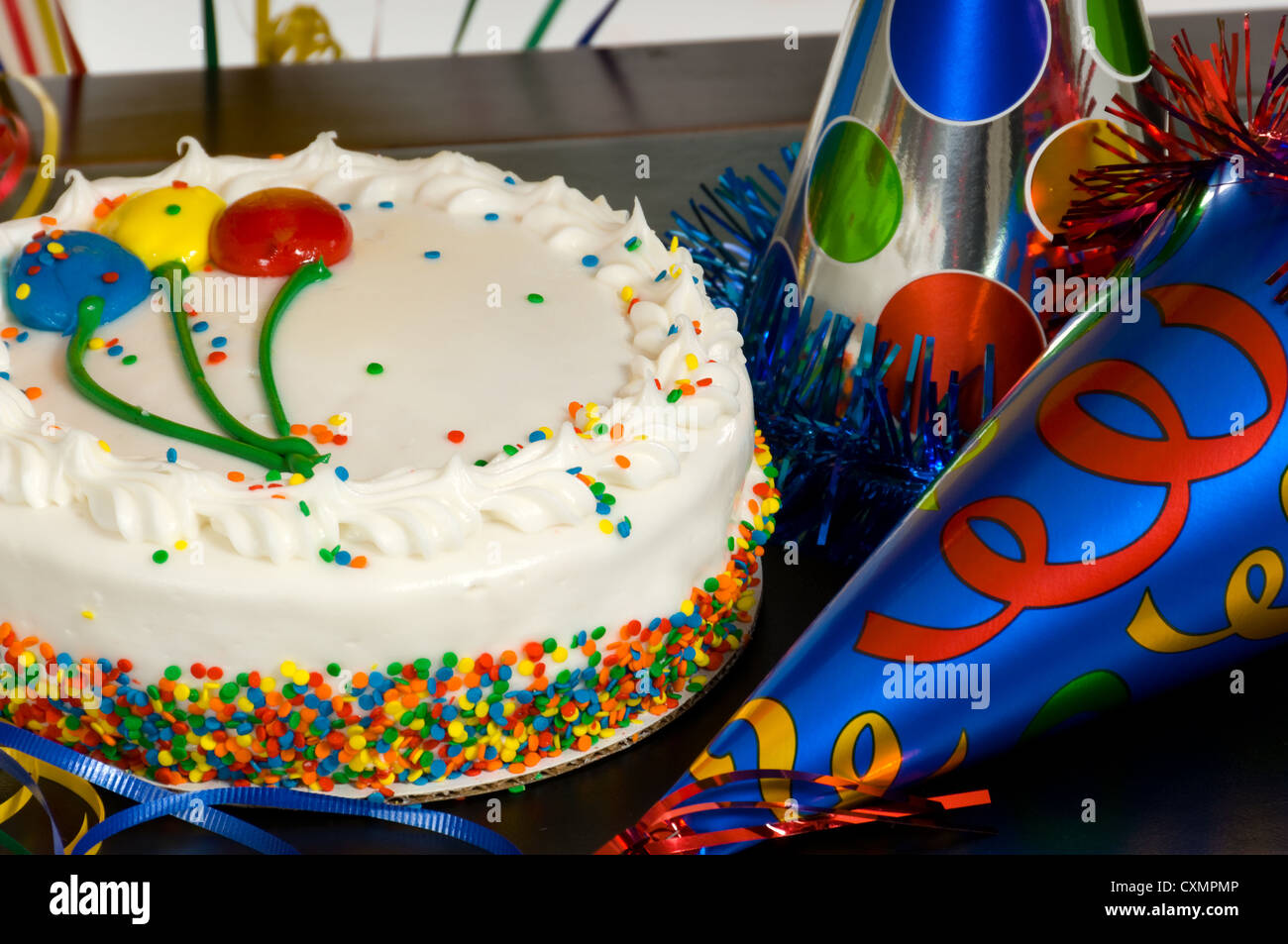 Birthday Cake with balloons on the icing and party hats on a table at a