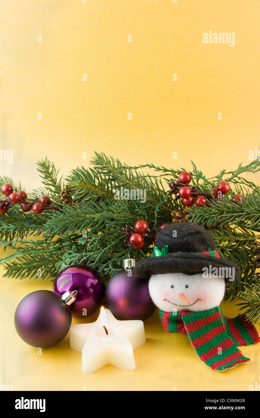 Christmas snowman with star shaped candle, purple baubles, fir branch on a solt gold background with copyspace Stock Photo