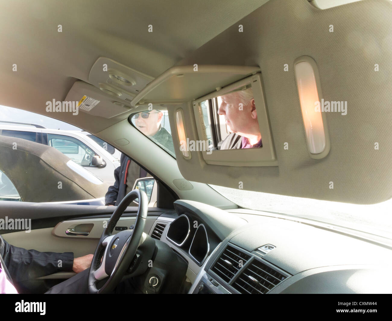 Driver's Reflection in Vehicle Vanity Mirror in Parking Lot Stock Photo