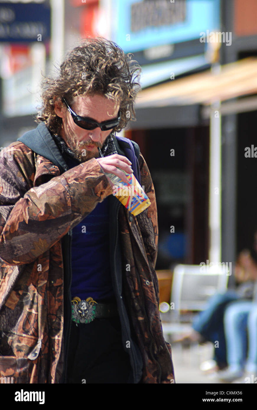 Scruffy man walking in the street with soft drink Stock Photo