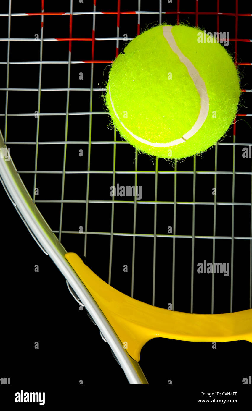 Yellow, green tennis ball resting on strings of a racket against black ...
