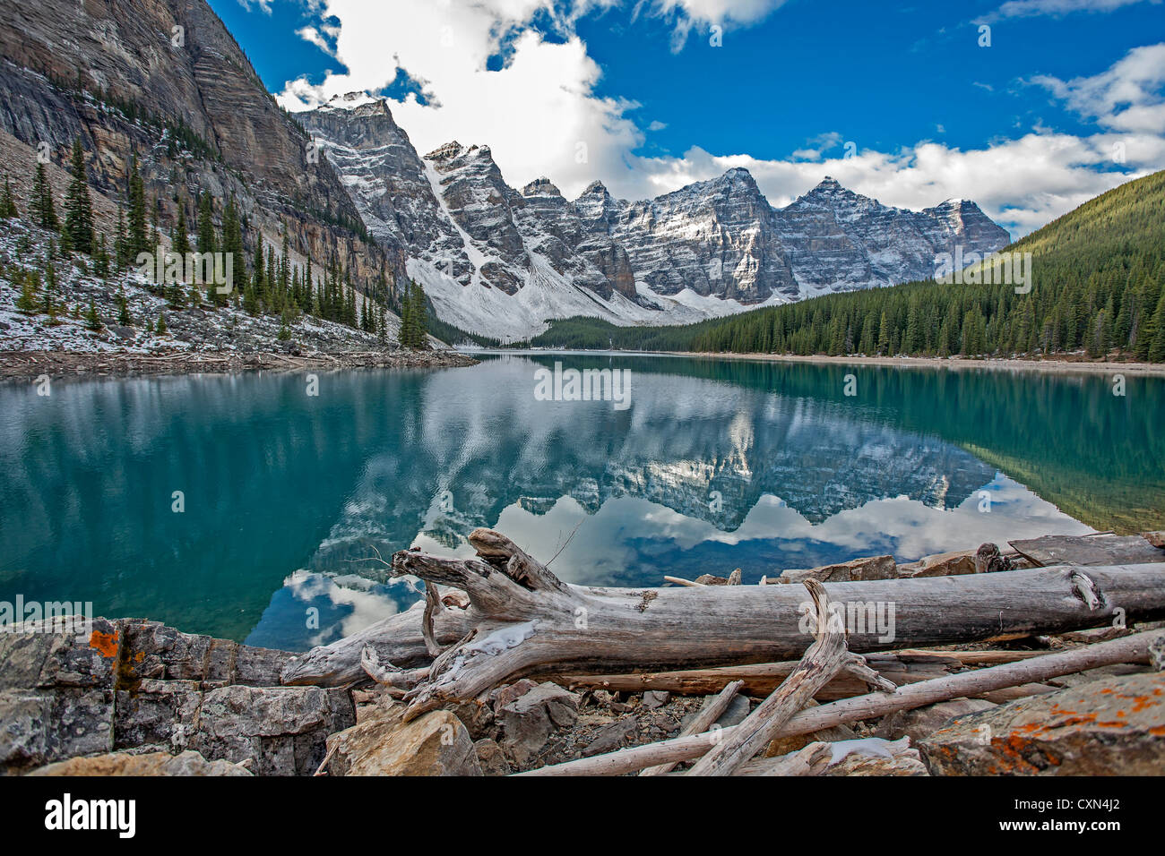 Lake Moraine glacial fed mountain pond with driftwood in forefront and mountain peaks in the background Stock Photo