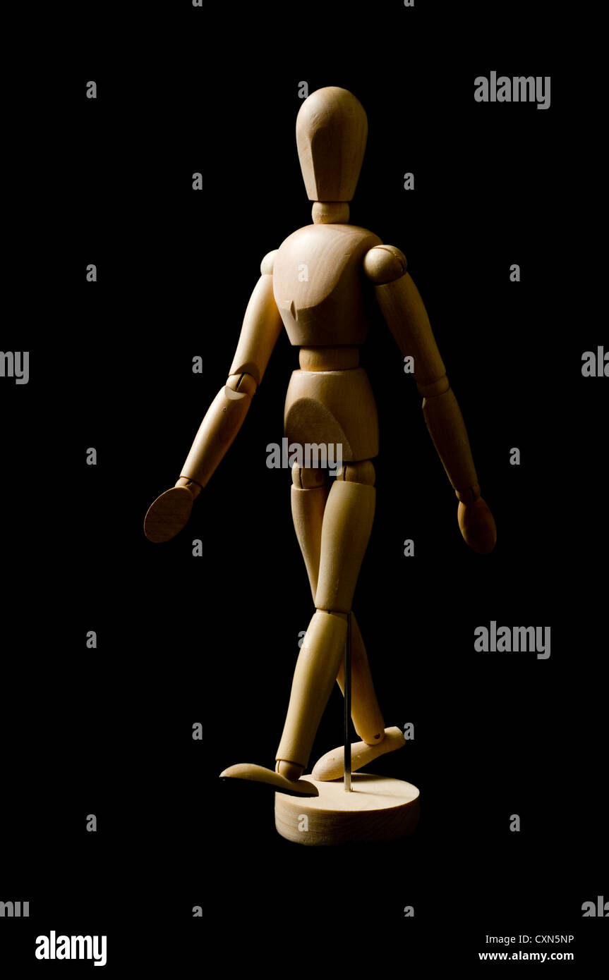 Artist person posing doll in walking gesture on black background, lit from the side to provide shape Stock Photo